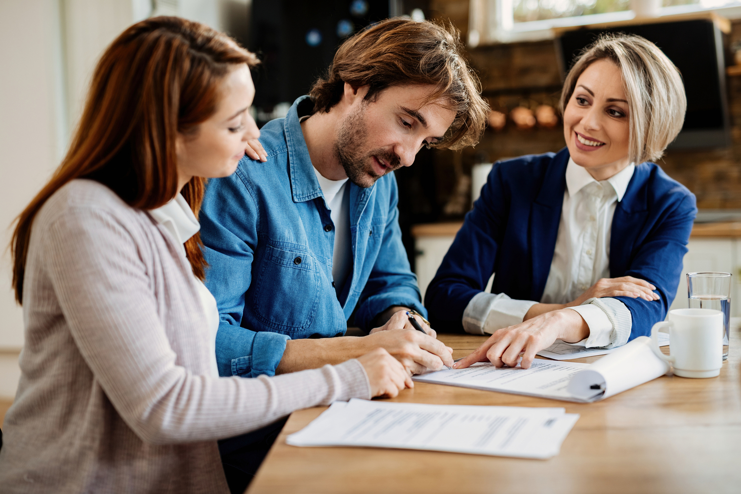 Young couple signing lease agreement while having meeting with real estate agent. Focus is on man.
